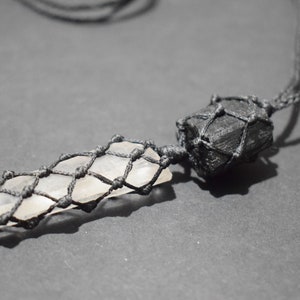 May include: A black cord necklace with a clear crystal point wrapped in black macrame and a black stone wrapped in black macrame.