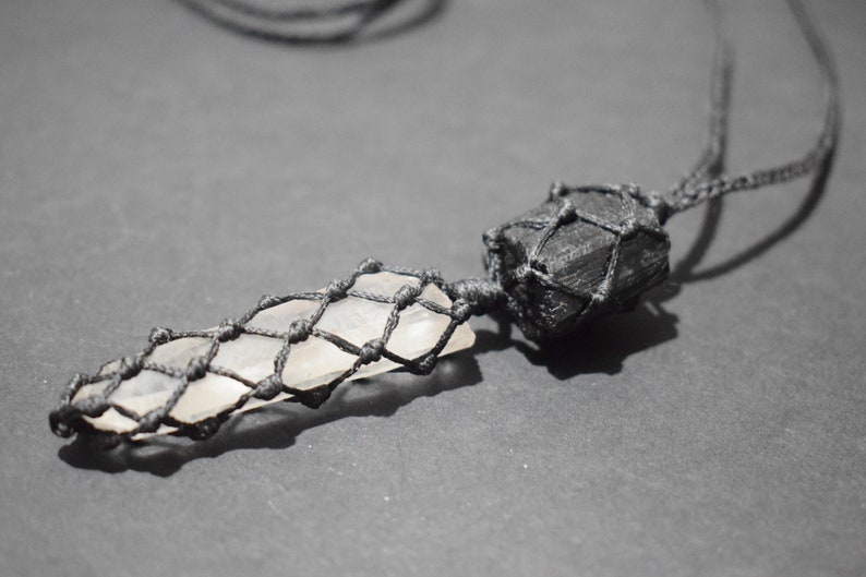 May include: A black cord necklace with a clear crystal point wrapped in black macrame and a black stone wrapped in black macrame.