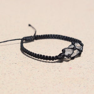 May include: A black braided bracelet with a clear quartz crystal wrapped in the cord.