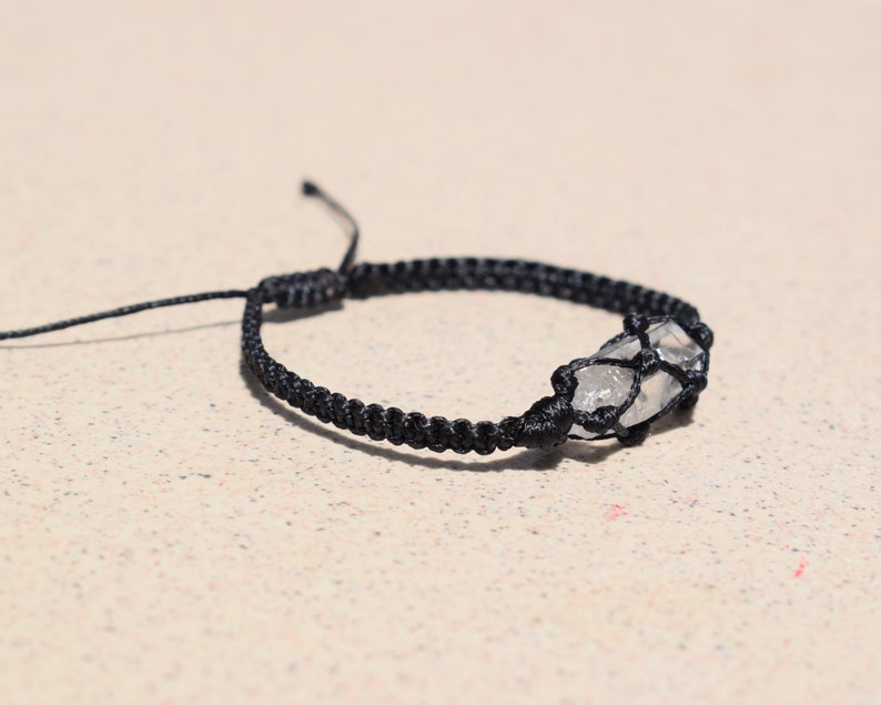 May include: A black braided bracelet with a clear quartz crystal wrapped in the cord.