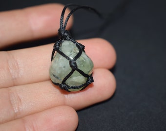 May include: A green crystal stone pendant wrapped in black cord, hanging from a black cord necklace.