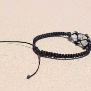 May include: A black braided bracelet with a clear quartz crystal wrapped in the braid.