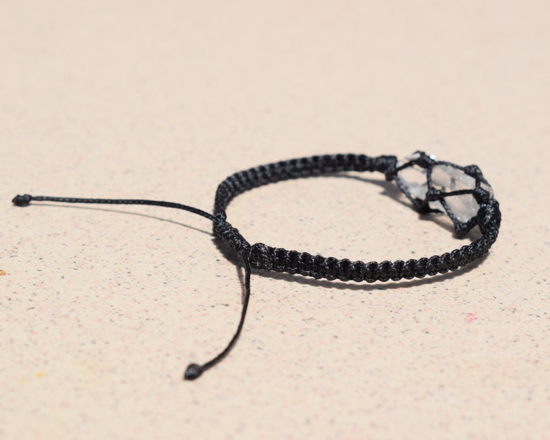 May include: A black braided bracelet with a clear quartz crystal wrapped in the braid.