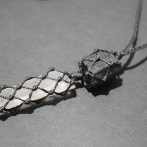 May include: A black cord necklace with a clear crystal pendant wrapped in black macrame. The crystal is shaped like a long, thin point.