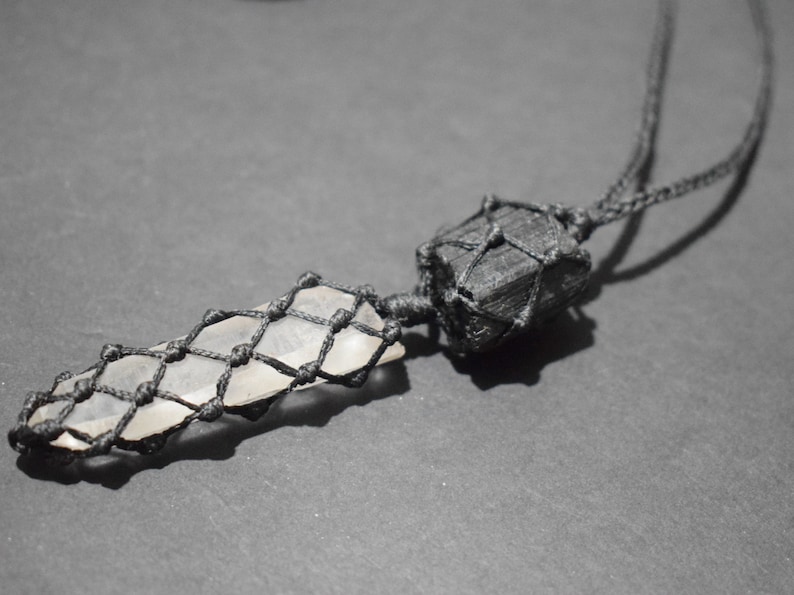 May include: A black cord necklace with a clear crystal pendant wrapped in black macrame. The crystal is shaped like a long, thin point.