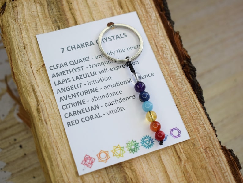 May include: A keychain with seven chakra crystals, each representing a different color of the rainbow. The crystals are strung on a black cord and attached to a silver key ring. The card attached to the keychain lists the crystals and their corresponding chakra meanings.
