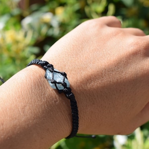 Può includere: Un braccialetto in macramé nero con un ciondolo di cristallo blu chiaro.