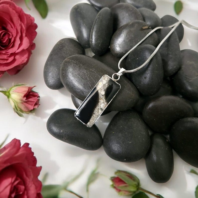 May include: A silver chain necklace with a rectangular pendant featuring black and white agate. The pendant is set in a clear resin and has a swirling pattern.
