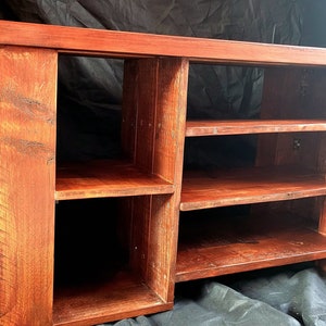 May include: A rustic wooden entertainment center with four shelves and a dark reddish-brown stain. The shelves are open and the unit has a simple design.
