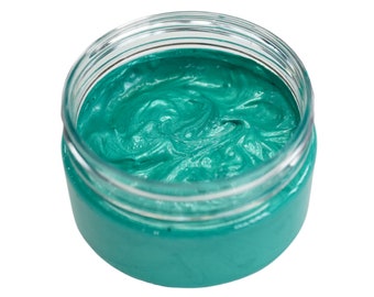 Può includere: Un barattolo di vetro trasparente pieno di vernice color verde acqua. La vernice ha una consistenza a spirale e il barattolo è aperto, rivelando il contenuto. La vernice appare densa e cremosa, con una leggera lucentezza.