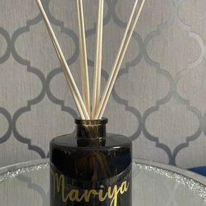 May include: Black glass diffuser bottle with gold lettering that reads "Mariya" and wooden diffuser sticks.