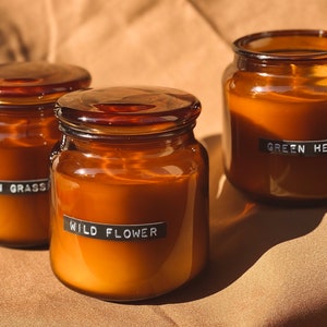 May include: Three amber glass candle jars with black labels. The labels read "Lemon Grass", "Wild Flower", and "Green Herbs".