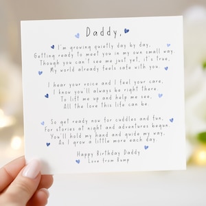 May include: A white card with the words "Daddy," and a poem in blue ink. The card is held by a person. The card is a birthday greeting from a baby to their father.