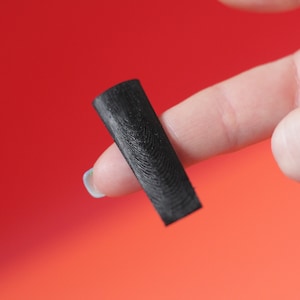 Op de afbeelding: Een zwarte, rechthoekige gitaarplectrum met een getextureerd oppervlak.