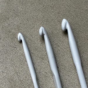 May include: Three white crochet hooks of varying sizes arranged side by side. Each hook features a smooth, tapered shaft and a curved head designed for yarn manipulation. The hooks are uniform in color, showcasing a clean, matte white finish throughout.