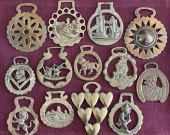 Puede incluir: Una colección de trece adornos de latón para arneses de caballo con varios diseños, incluyendo el castillo de Warwick, el Tower Bridge, un barco, un caballo, un león, un duende y un arreglo en forma de corazón. Cada pieza tiene una anilla.