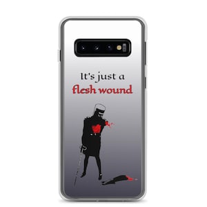 以下が含まれることがあります： 赤いハートと剣を持った騎士の黒いシルエットが描かれた透明な携帯電話ケース。騎士は腕が1本なく、ケースには「It's just a flesh wound」という文字が印刷されています。