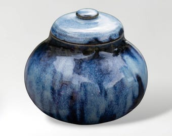 Könnte beinhalten: Eine Keramikdose mit Deckel und blauer Glasur. Die Dose hat eine runde Form mit einem Deckel und einem kleinen Knauf. Die blaue Glasur hat einen Marmoreffekt, mit dunkleren Farbtönen am Boden und helleren Farbtönen auf dem Deckel.