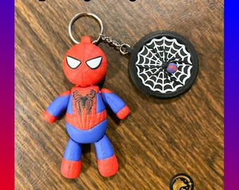 May include: A red and blue Spider-Man keychain with a black web design. The keychain features a small, round, black web charm with a red spider in the center.