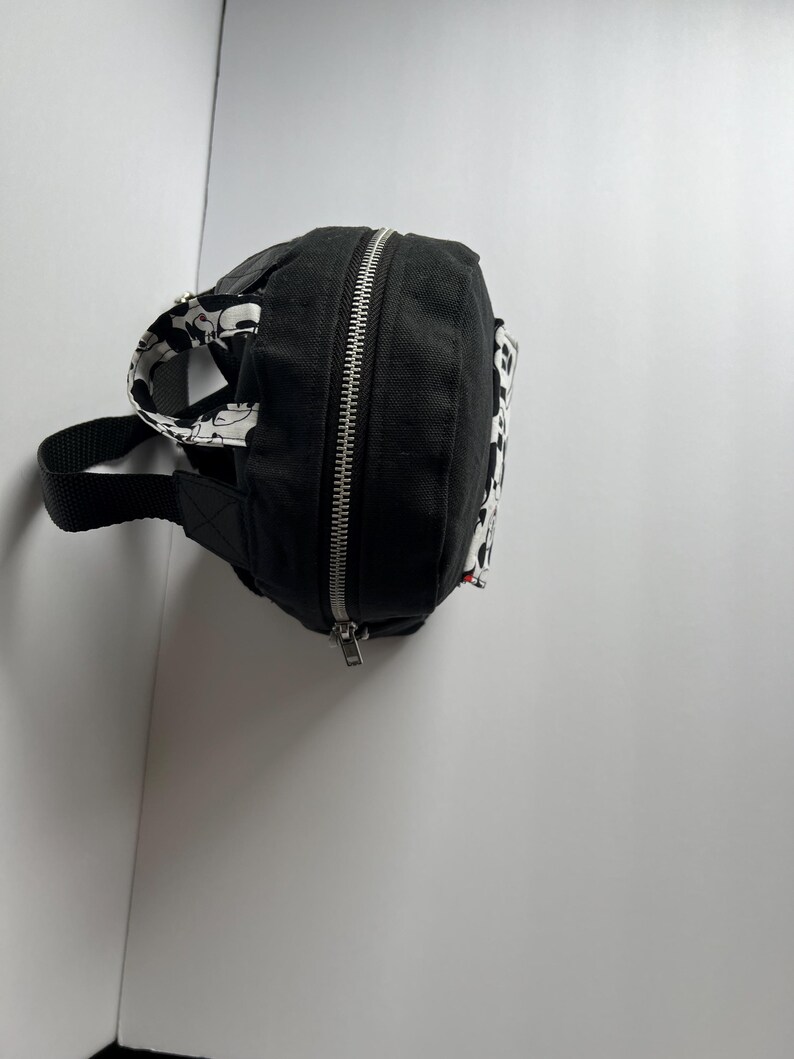 May include: Black fanny pack with a silver zipper and a black strap. The pack features a black and white patterned design on the sides and strap. The fanny pack is made of a durable material.