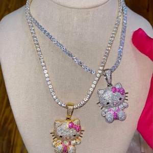 May include: Two gold chains with diamond-encrusted Hello Kitty pendants. The pendants have pink bows and are on a white mannequin.