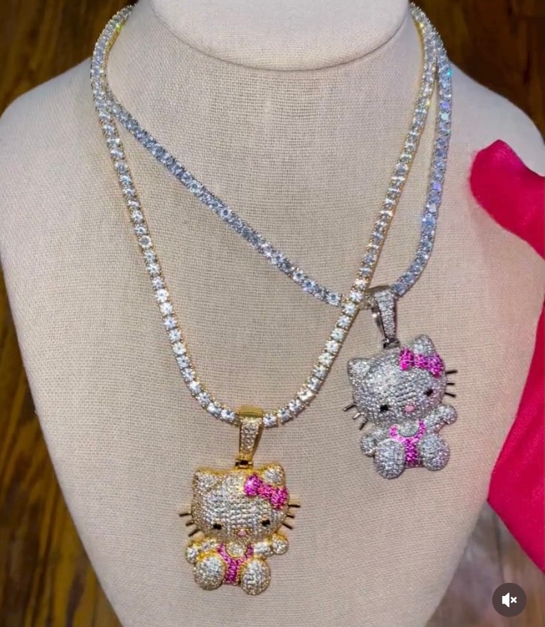 May include: Two gold chains with diamond-encrusted Hello Kitty pendants. The pendants have pink bows and are on a white mannequin.