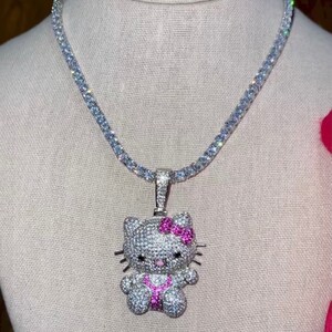 May include: A silver chain necklace with a white and pink Hello Kitty pendant. The pendant is covered in small clear stones and has a pink bow.