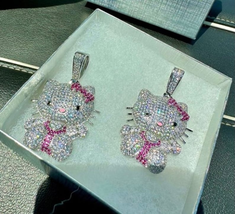 May include: Two silver Hello Kitty pendants with pink bows and rhinestones. The pendants are in a white box with a gray lining.