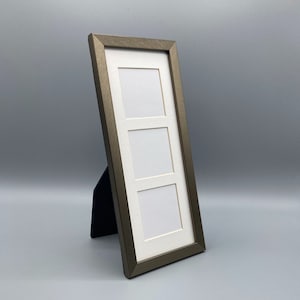 May include: A rectangular, bronze-colored triple photo frame with three white mat openings. The frame is angled and supported by a black easel back. The frame is designed to hold three photos.
