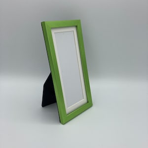 May include: A green picture frame with a white mat and a stand. The frame is made of wood and has a smooth finish.