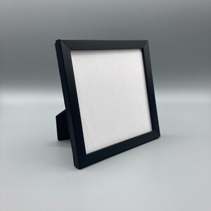May include: A black picture frame with a white mat and a stand on the back. The frame is empty.