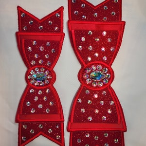 May include: Two red velvet bows with large, clear rhinestones and a single larger, iridescent rhinestone in the centre of each bow.