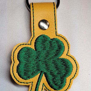 May include: A yellow leather keychain with a green embroidered shamrock.