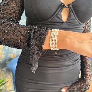 May include: A multi-strand pearl bracelet with a gold chain clasp. The bracelet features several rows of small, round, white pearls. The clasp is a delicate gold chain. The bracelet is worn on a wrist.