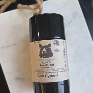 May include: A black deodorant stick with a label featuring a bear illustration. The label reads "Northern Bear Soap Natural Deodorant Blue Cypress" and lists ingredients. Net weight is 3.6oz.