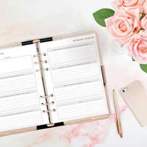 May include: An open planner with a beige cover and gold rings. The pages are filled with a printable scripture analysis worksheet. The worksheet includes prompts for reflection and journaling. The planner is on a white surface with a pink rose bouquet and a gold phone.