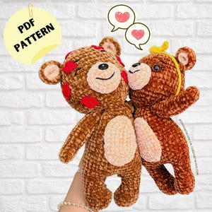 May include: Two brown crocheted teddy bears with red hearts on one bear. The bears are holding each other and have a loving expression on their faces. The bears are in front of a white brick wall.