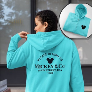 May include: A turquoise blue hooded sweatshirt with a black Mickey Mouse silhouette and the text "Please Return To Mickey & Co. Main Street, USA 1928" on the back.