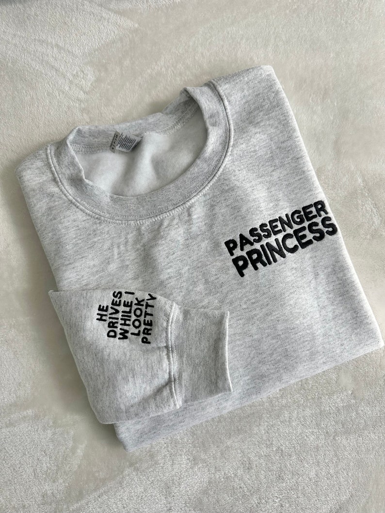 Op de afbeelding: Grijs sweatshirt met de tekst "Passenger Princess" aan de rechterkant en "He drives while I look pretty" op de linkermouw.