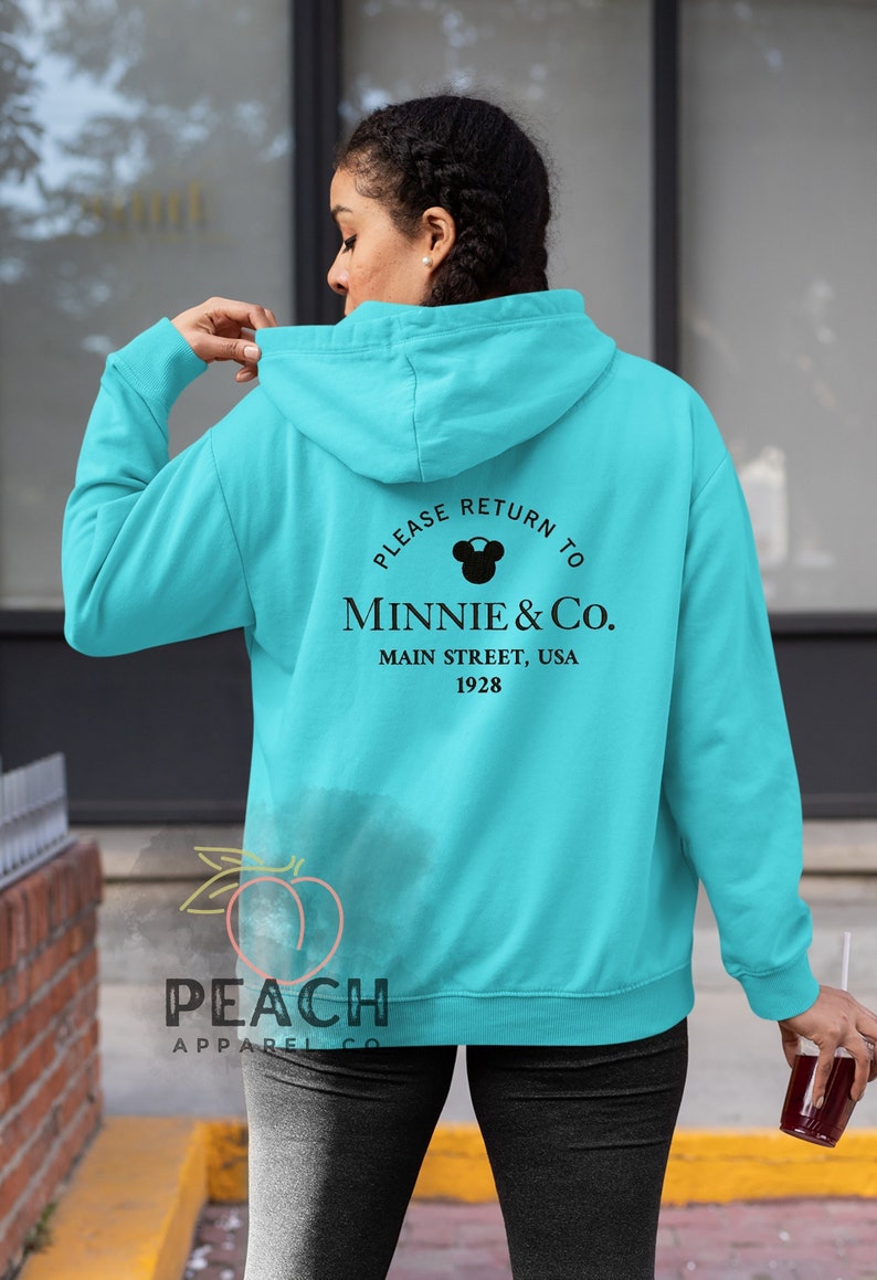 May include: A turquoise blue hoodie with a black graphic on the back that says "Please Return to Minnie & Co. Main Street, USA 1928".