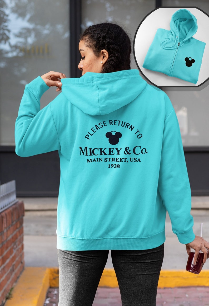May include: A turquoise blue hooded sweatshirt with a black Mickey Mouse silhouette and the text "Please Return To Mickey & Co. Main Street, USA 1928" on the back.