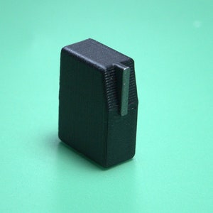 May include: A black plastic knob with a silver metal shaft. The knob is rectangular with rounded edges.