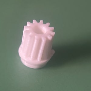 May include: White plastic gear with a round, toothed top and a cylindrical base.