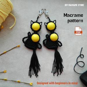 May include: Two black macrame cat keychains with yellow bead accents and silver clasps. Each keychain has a tassel and cat-ear details. The image includes text that says "DIY Macrame Store" and "Macrame pattern". The phrase "Designed with beginners in mind" is also visible.
