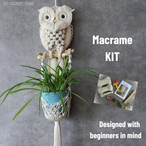 Op de afbeelding: Een macramé uil plantenhangerset met een blauwe pot met een groene plant. De uil is gemaakt van crèmekleurig macramé en hangt aan een houten deuvel. De tekst luidt "Macrame KIT" en "Designed with beginners in mind".