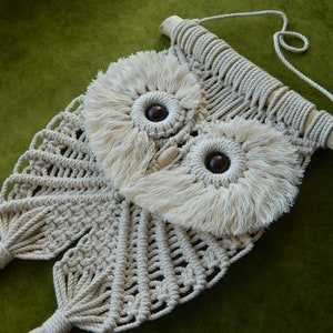 Peut inclure: Une suspension murale en macramé en forme de hibou blanche avec une baguette en bois et des perles en bois brun pour les yeux.