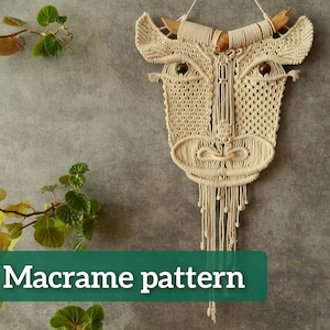 Può includere: Un arazzo da parete in macramè beige a forma di testa di toro. L'opera presenta corna di legno, occhi di perline marroni scuri e un design intrecciato strutturato. Il testo "Macrame pattern" è visualizzato su uno striscione verde.