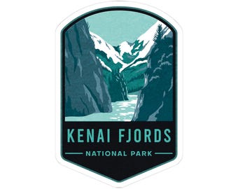 May include: A sticker featuring a scenic illustration of the Kenai Fjords National Park. The design showcases a mountain range with snow-capped peaks, a river, and the text "KENAI FJORDS NATIONAL PARK" in white and teal.