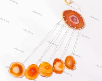 Puede incluir: Un carillón hecho de seis rodajas de ágata naranja, cada una con un patrón único. Las rodajas están suspendidas de un anillo de madera con finos cordones plateados.