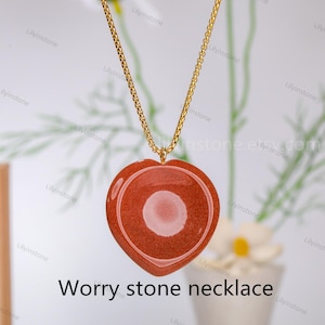 May include: A gold chain necklace with a heart-shaped red worry stone pendant. The stone has a smooth, polished surface.